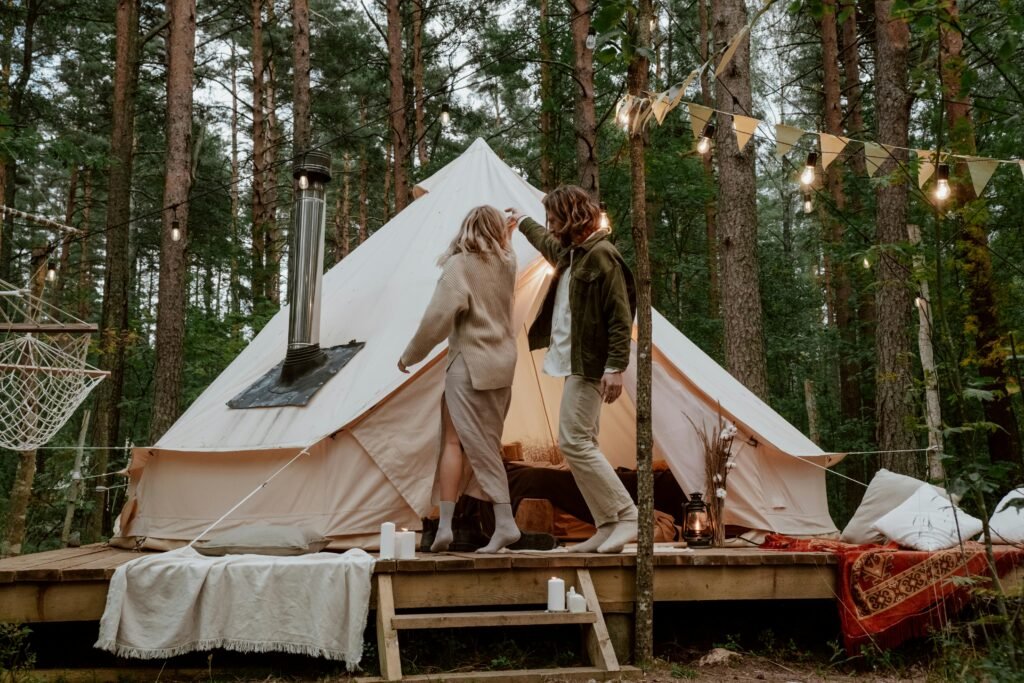 Couple enjoying a romantic evening at a glamping tent in a serene forest setting.